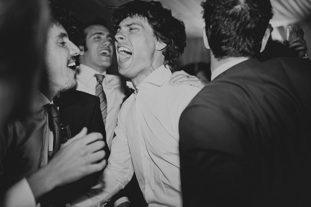 Energetic black and white candid shot of wedding reception guests dancing and laughing.