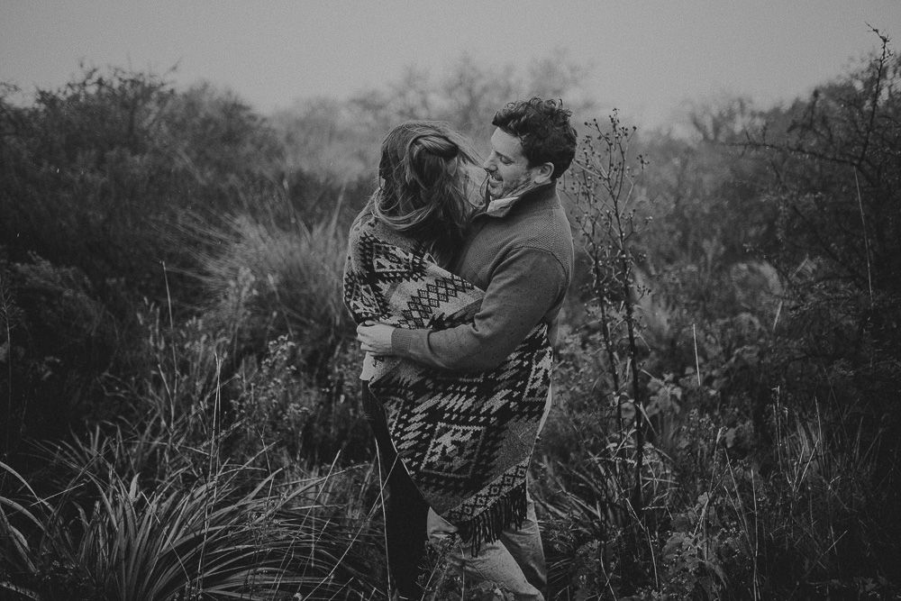 Couple wrapped in blanket share intimate embrace in wild natural setting.