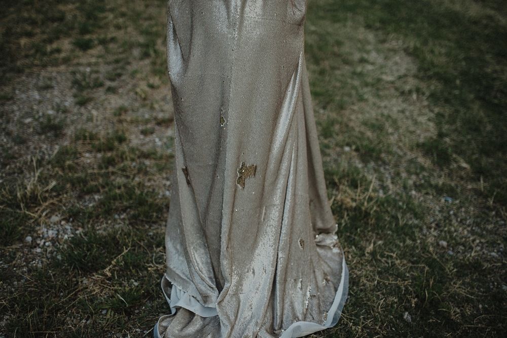 Detail shot of flowing silk wedding dress fabric against green grass.