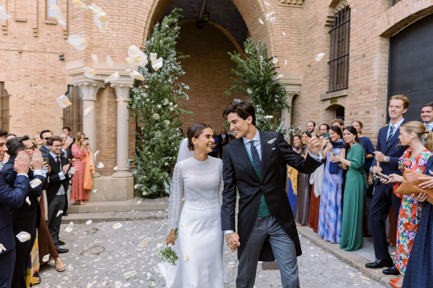 A joyful wedding exit through an archway lined with guests throwing flower petals.