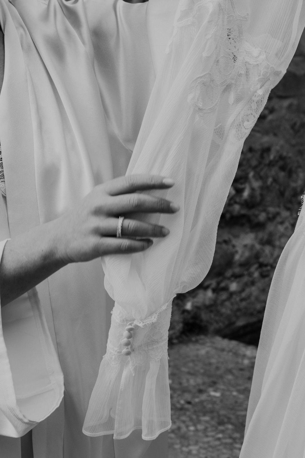 A black and white detail shot of a hand with wedding ring holding delicate bridal fabric.