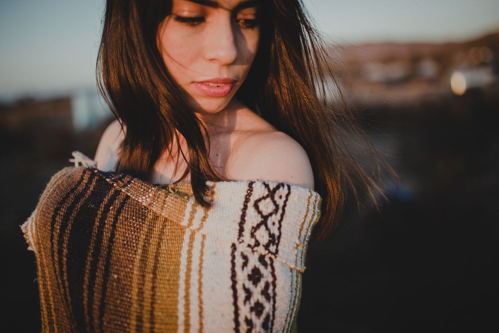 A person wearing a cozy patterned sweater poses at sunset with warm lighting and shallow depth of field.