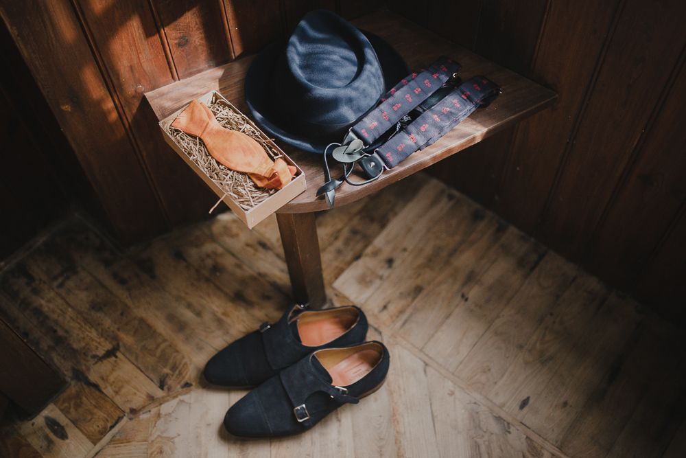 Black formal shoes and accessories arranged on wooden flooring in moody lighting.