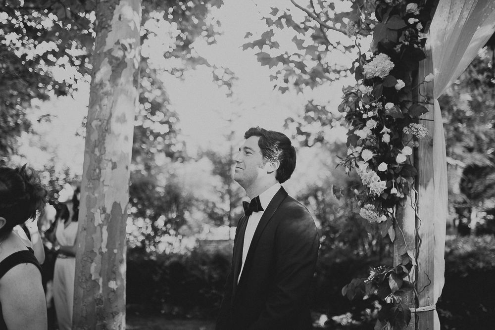 Groom stands under trees during an outdoor wedding ceremony.
