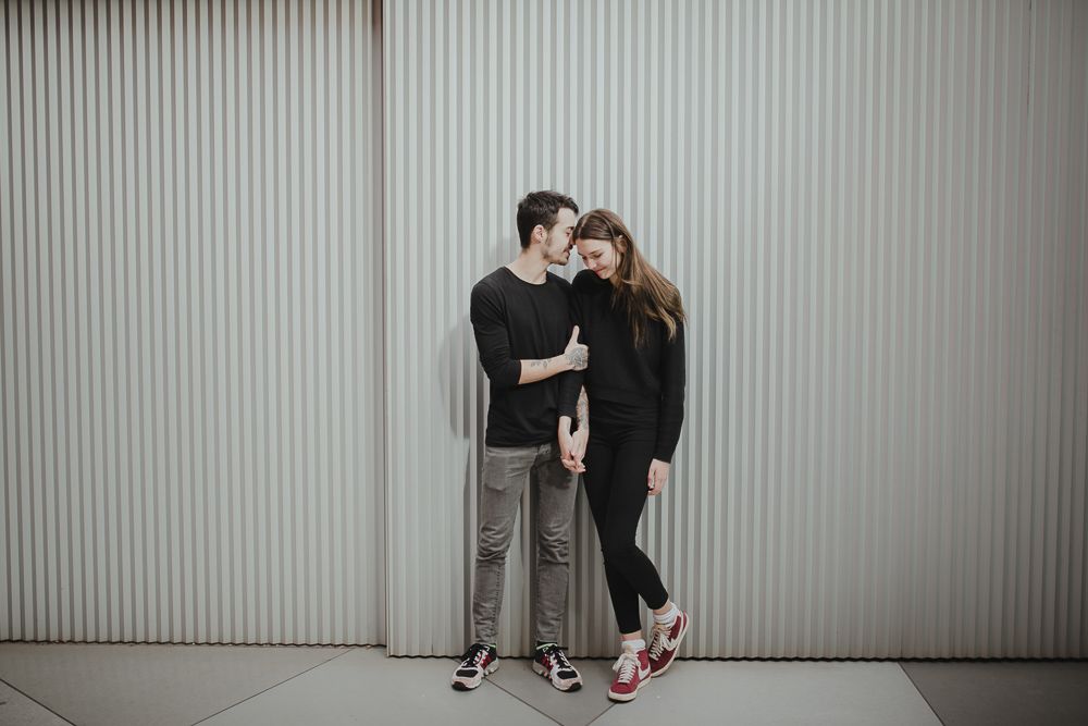 A couple shares an intimate moment against a white corrugated wall.