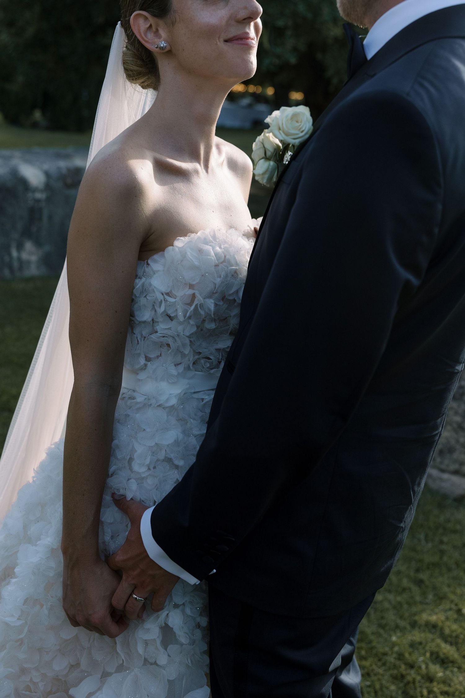A romantic wedding moment showing the bride in a detailed lace gown holding hands with her groom outdoors.