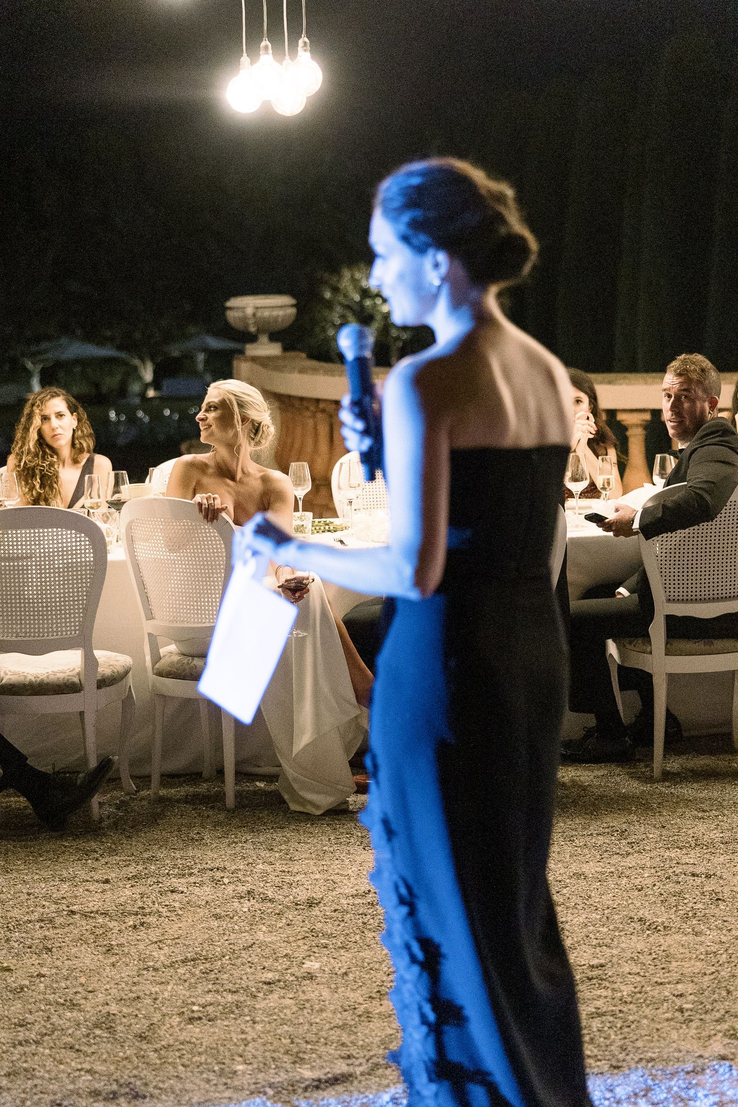 Evening outdoor wedding reception with dramatic blue lighting and white chairs.