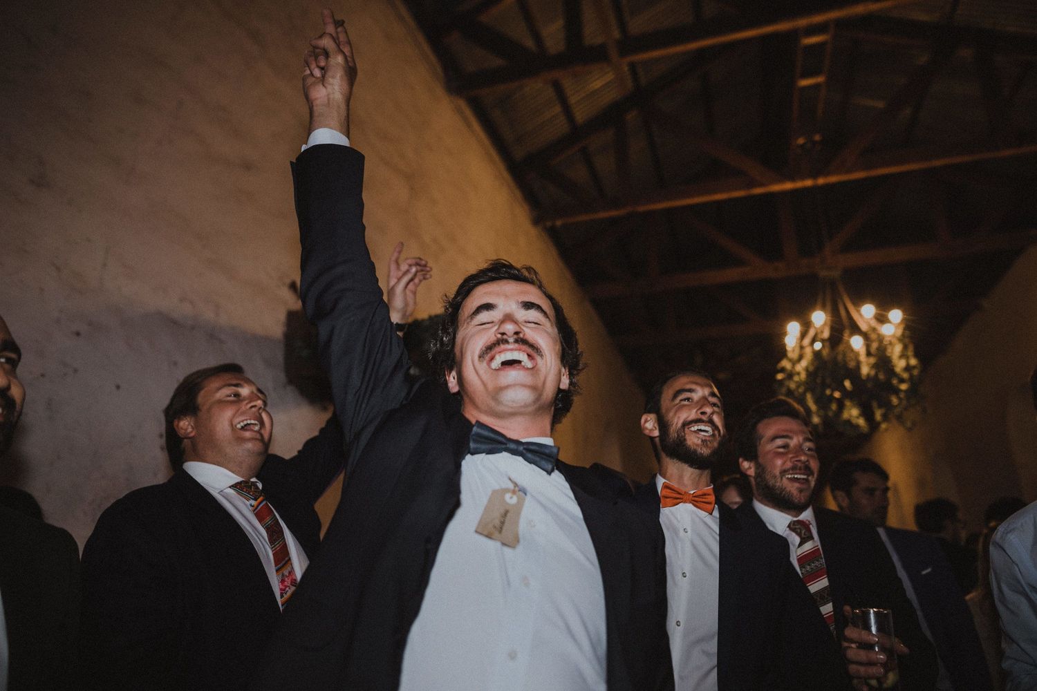 Joyful guests celebrate with raised arms at an elegant indoor venue with chandelier.
