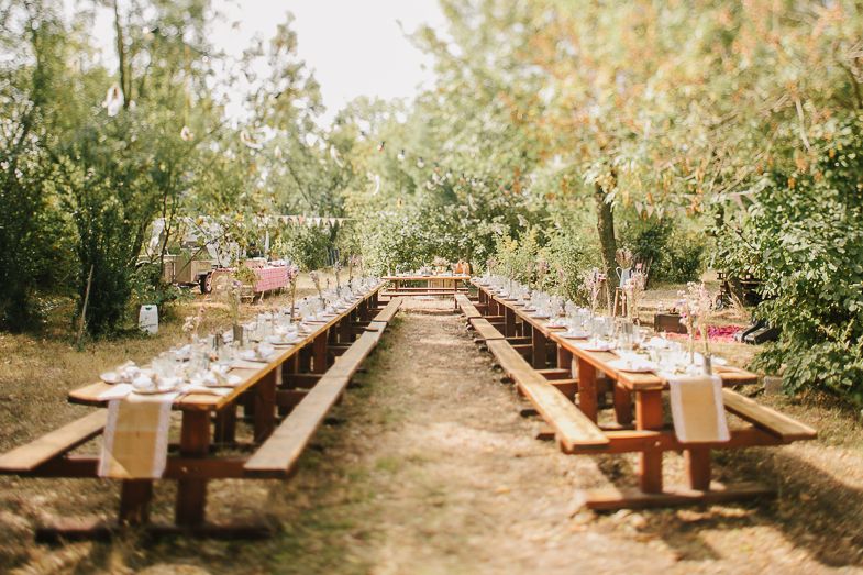 Long wooden tables set up outdoors for a wedding reception with place settings.