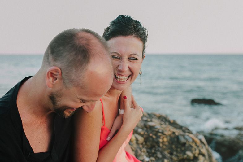 Candid beach portrait of a joyful couple sharing a laugh by the ocean.