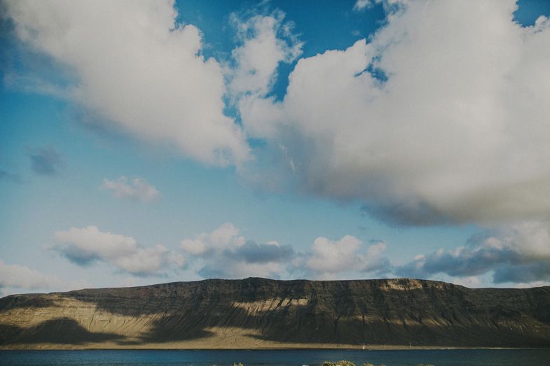 Scenic mountain landscape with calm waters under fluffy clouds and blue sky.