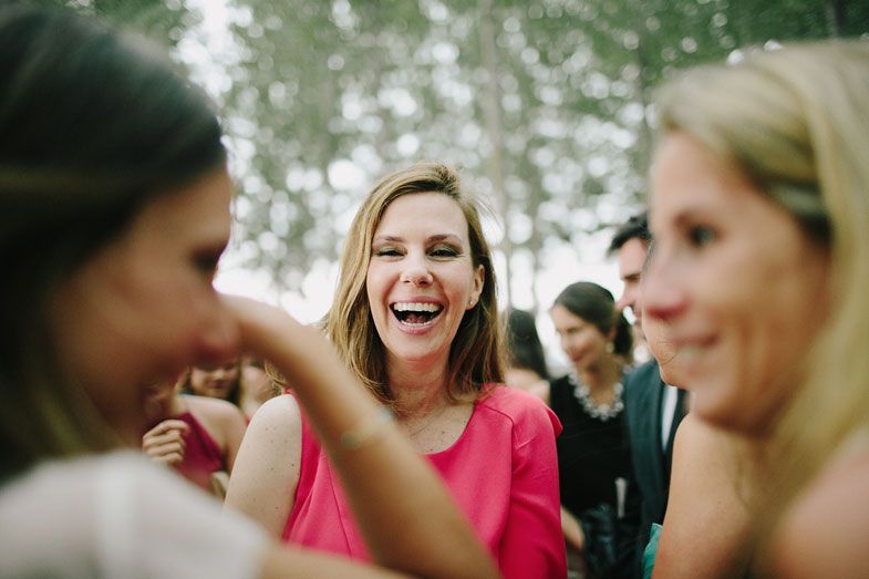 A group of wedding guests laugh and celebrate during an outdoor daytime reception.