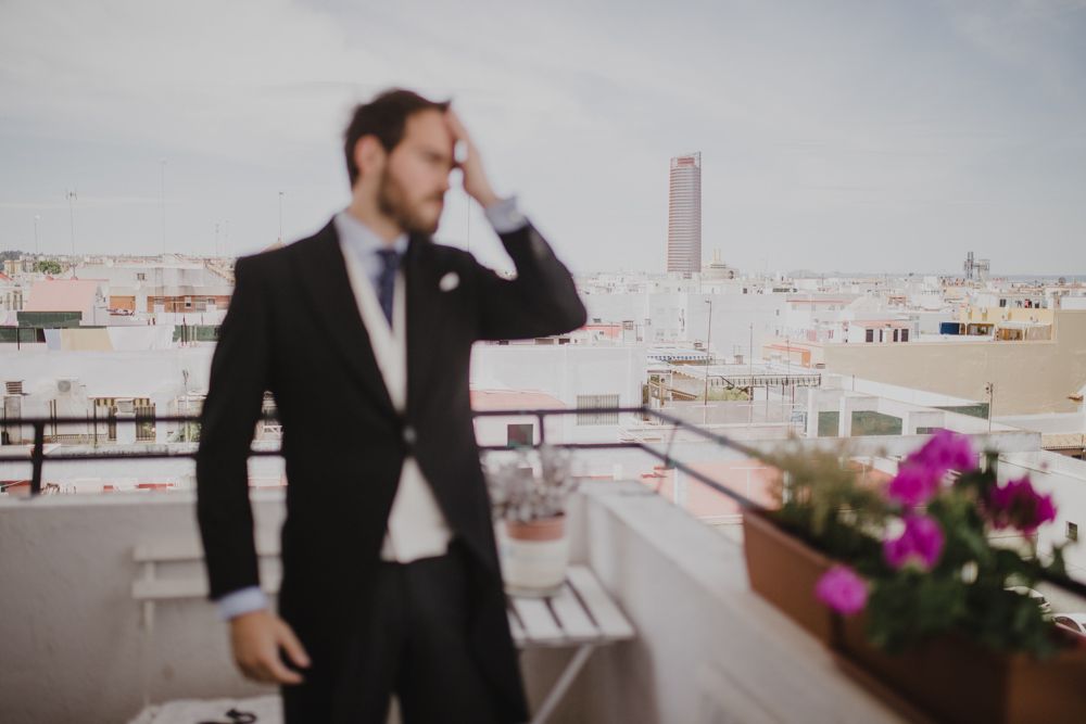 A suited figure stands on a rooftop terrace with urban skyline and pink flowers.