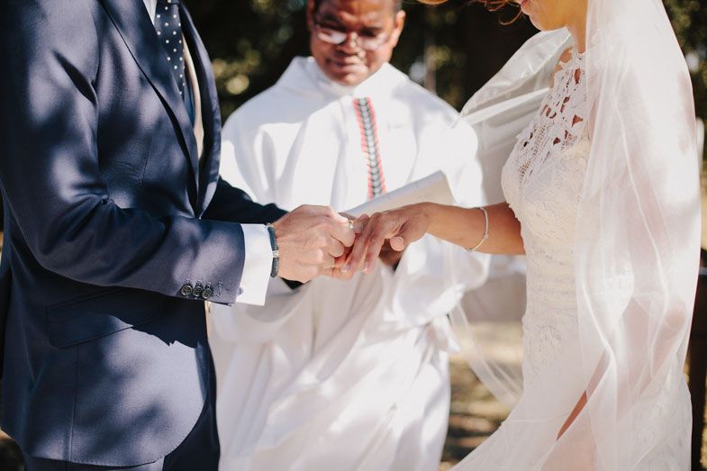 Close-up of hands exchanging rings during a wedding ceremony with white robed officiant present.