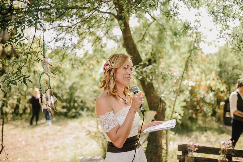 A speaker delivers remarks during a sunny outdoor garden wedding ceremony.