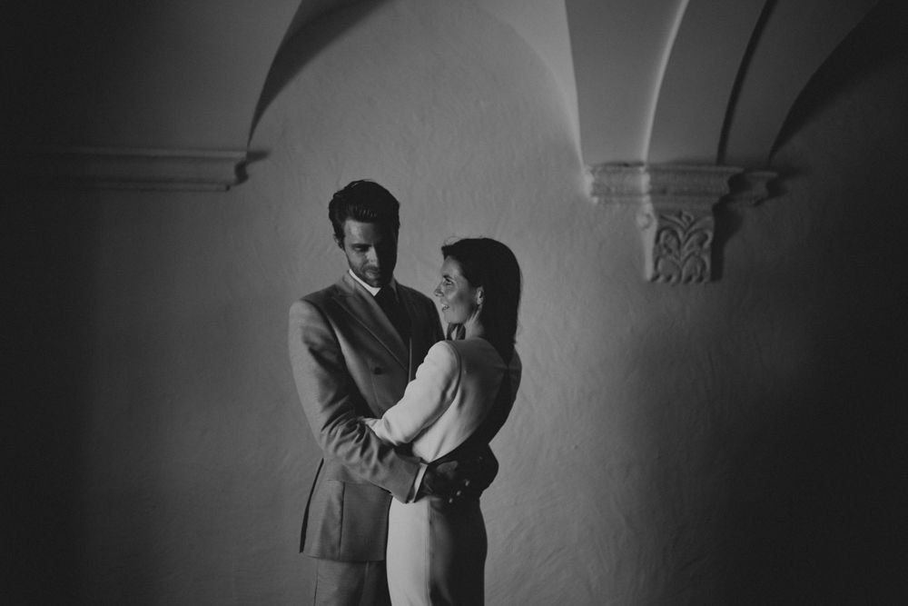 Dramatic black and white photo of couple in formal wear under ornate arches.