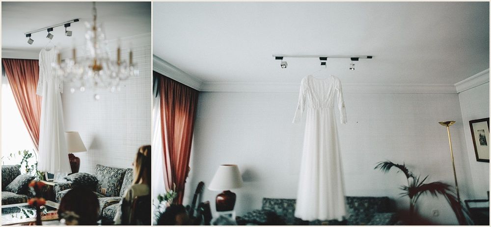 White wedding dress hangs elegantly from ceiling against draped coral curtains and chandelier.