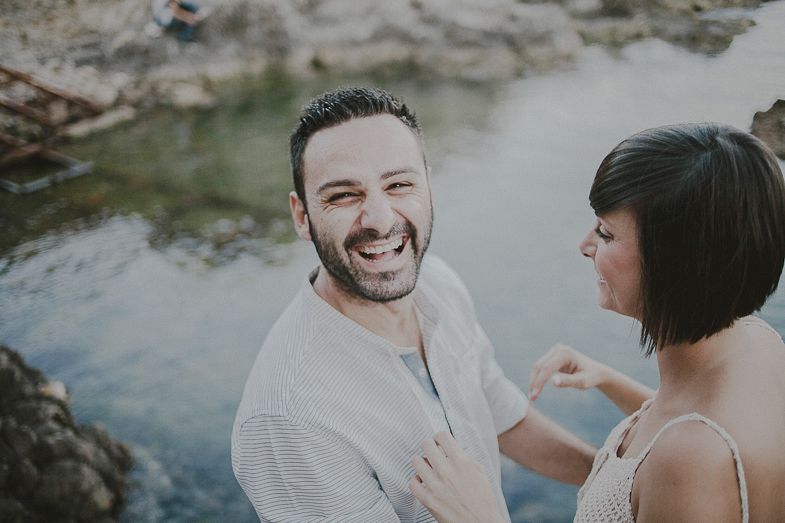 A couple shares a joyful moment together near a rocky coastline.