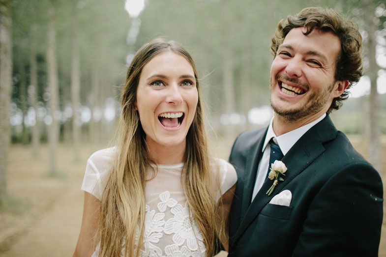 Joyful couple shares a candid laughing moment during their forest wedding photoshoot.