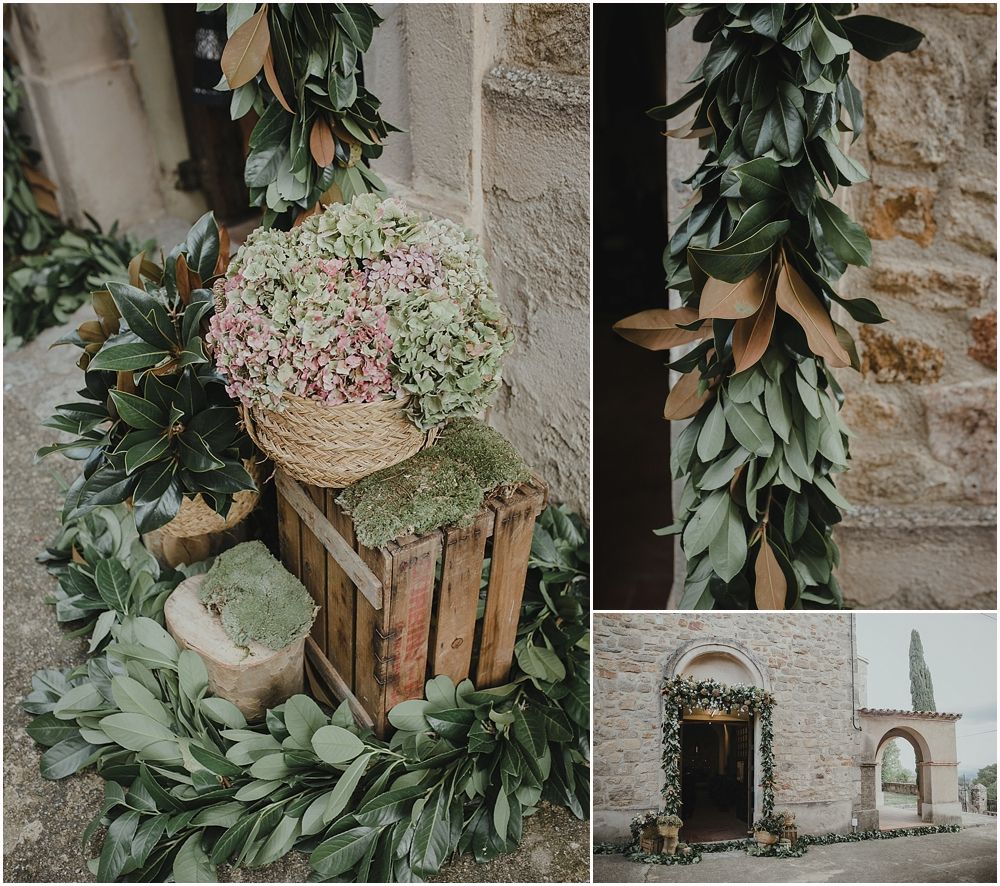 Wedding venue decorated with rustic wooden crates, greenery garlands, and delicate pink flowers against stone walls.