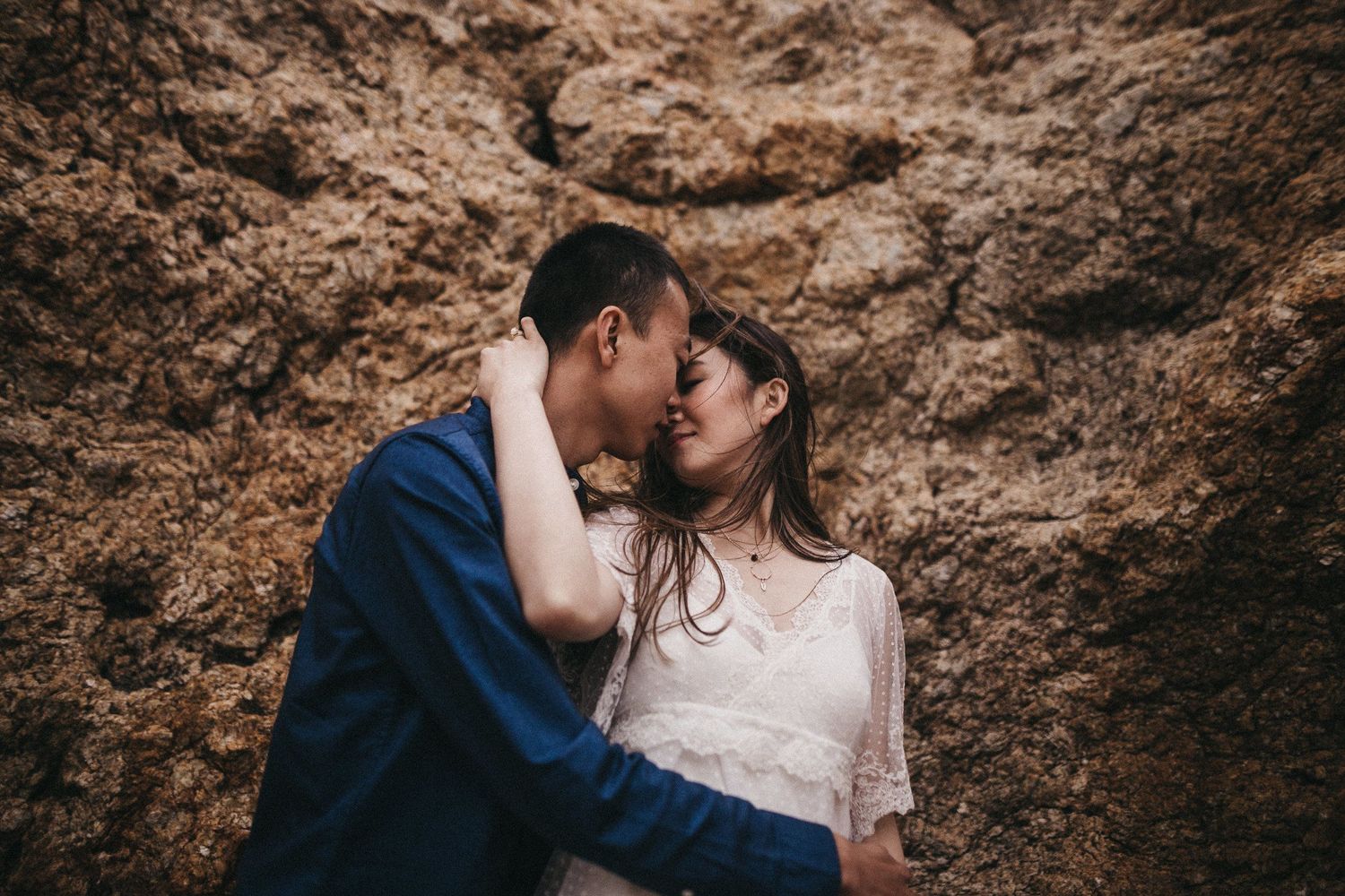 Romantic moment captured against a textured rock wall backdrop.