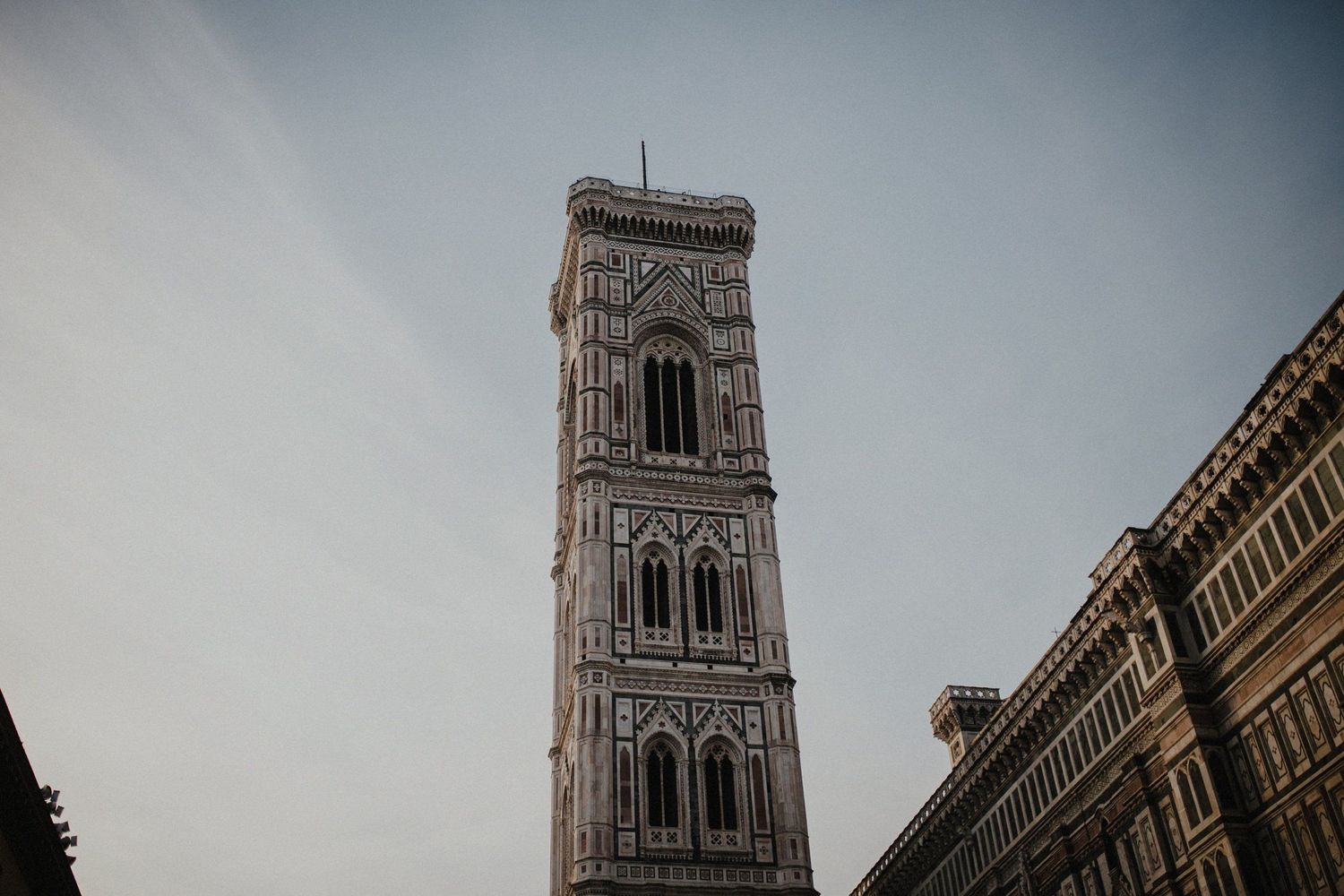 Towering stone bell tower of Florence's Duomo cathedral with ornate Gothic architectural details against cloudy sky.