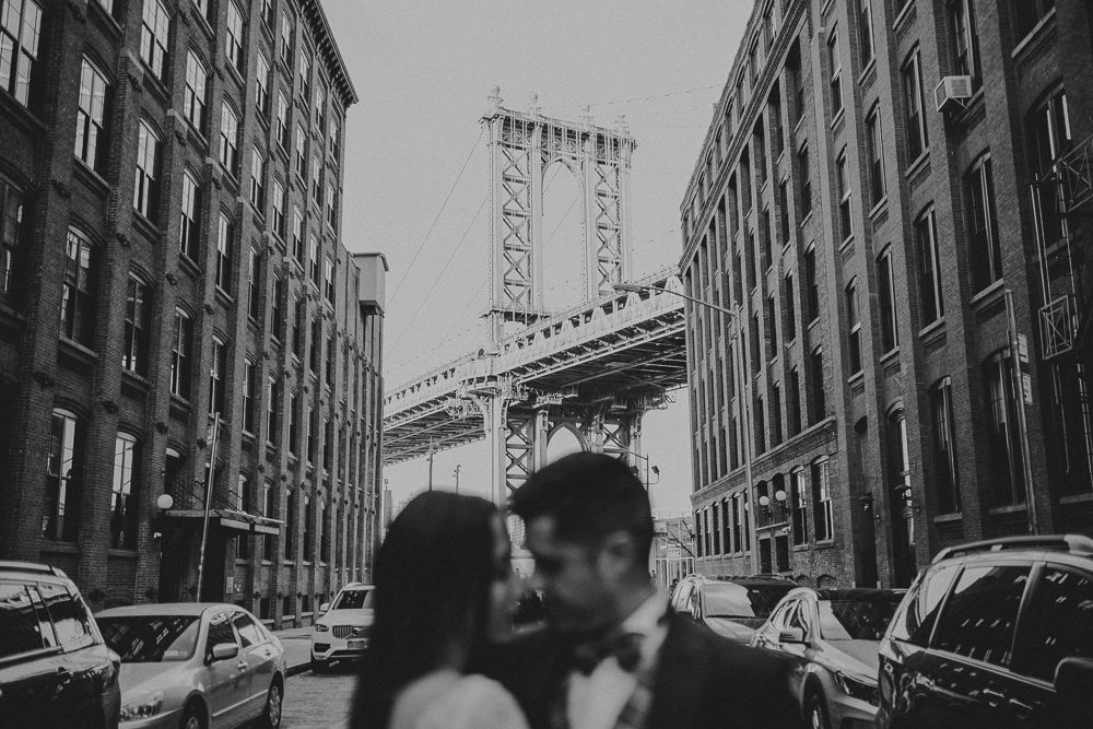 Black and white urban photo of Manhattan Bridge framed by classic New York buildings.