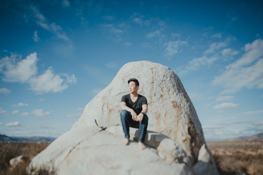 Person sits on large white boulder formation against desert mountain landscape.