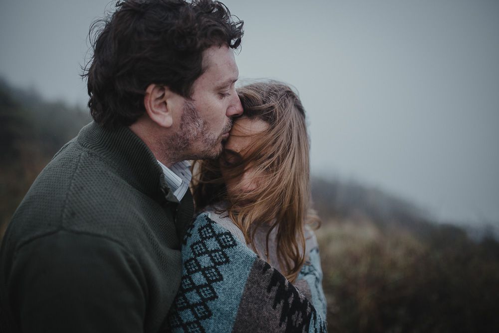 An intimate moment captured between a couple in warm winter clothing on a cloudy day.