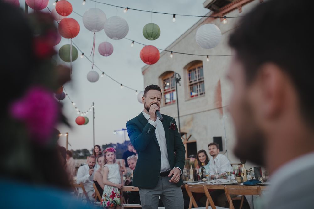 Wedding reception speech under colorful paper lanterns during an outdoor celebration.