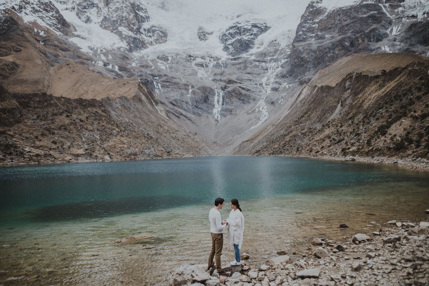 Travelers admire the pristine waters of an alpine lake beneath towering snow-covered peaks.