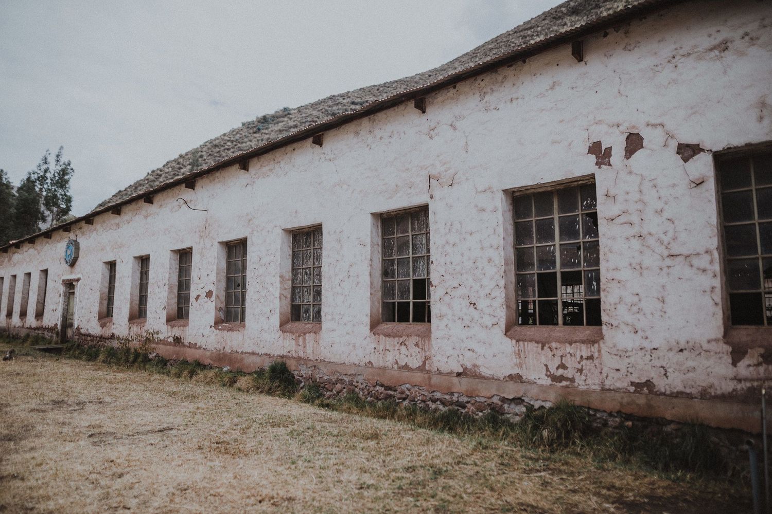 Long white building with fading pink walls and multiple windows in a desert setting.