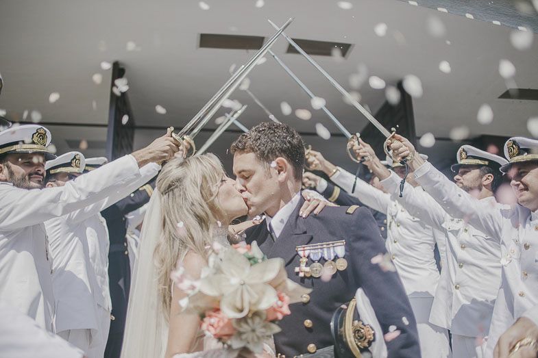 Military officers form a sword arch over a couple sharing a kiss on their wedding day amidst falling snow.