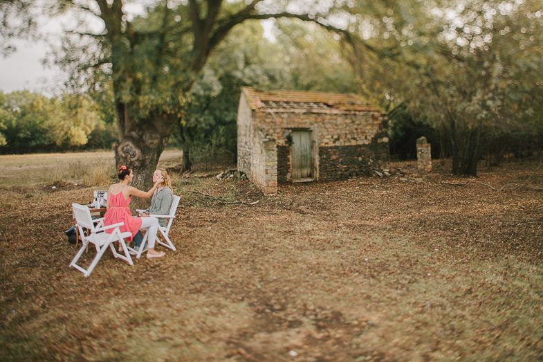 Outdoor gathering with white chairs and rustic stone building in a wooded setting.