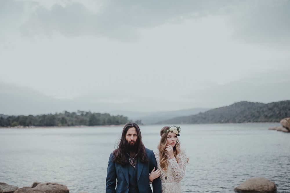 A couple shares a tender moment on the rocky shore of a serene mountain lake.