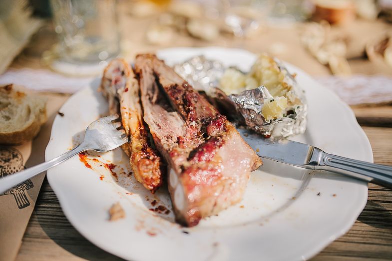 A plate with partially eaten grilled meat and seafood at a rustic outdoor dining setting.