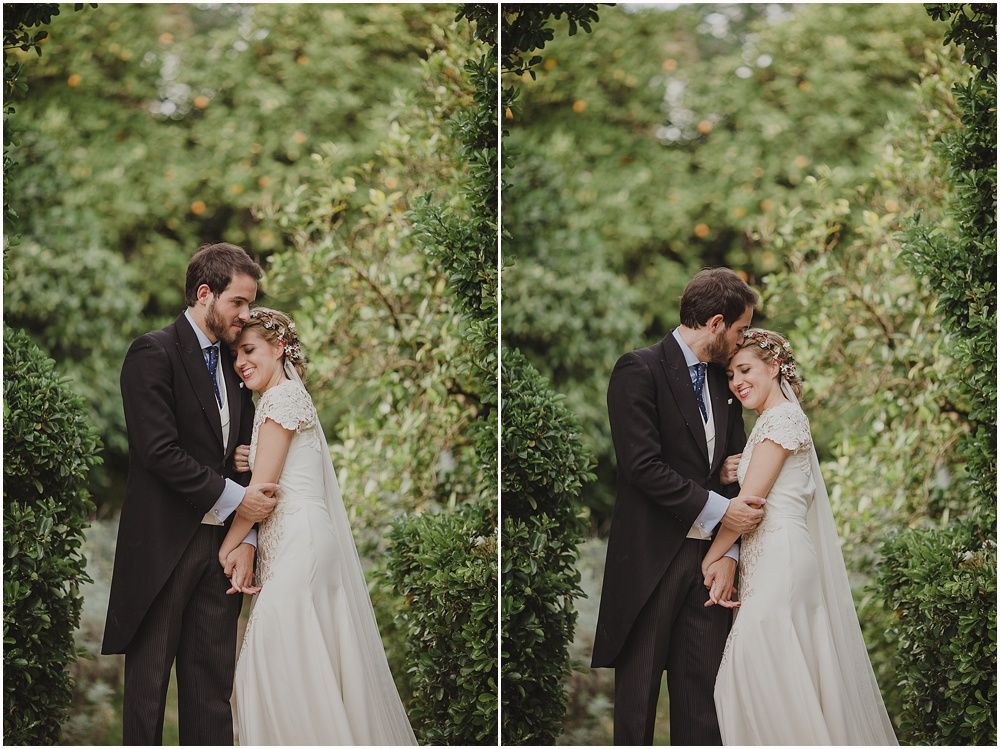 Two newlyweds share an intimate moment in a lush garden setting with greenery in the background.