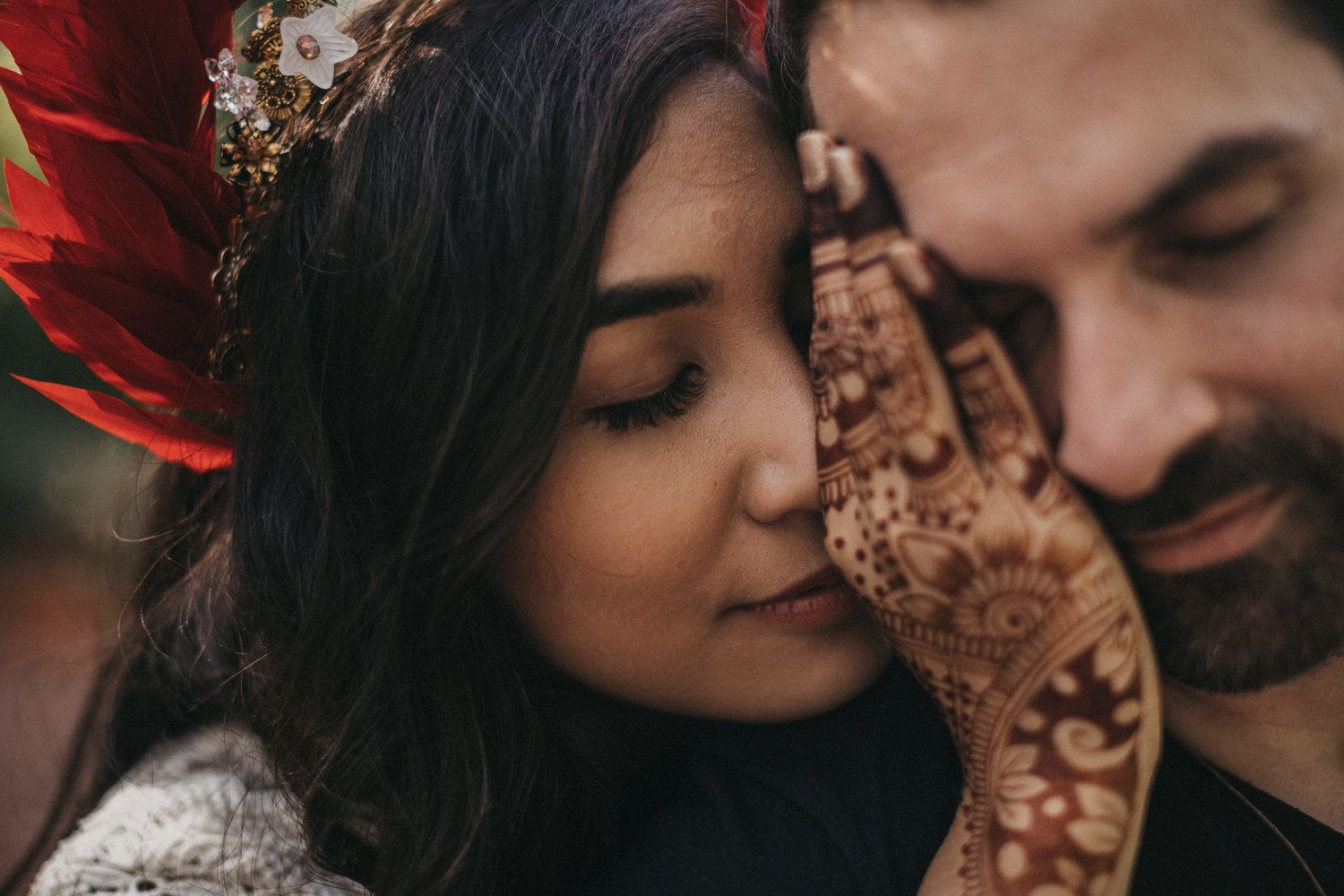 Close up of intricate henna design on hands with romantic couple embrace.