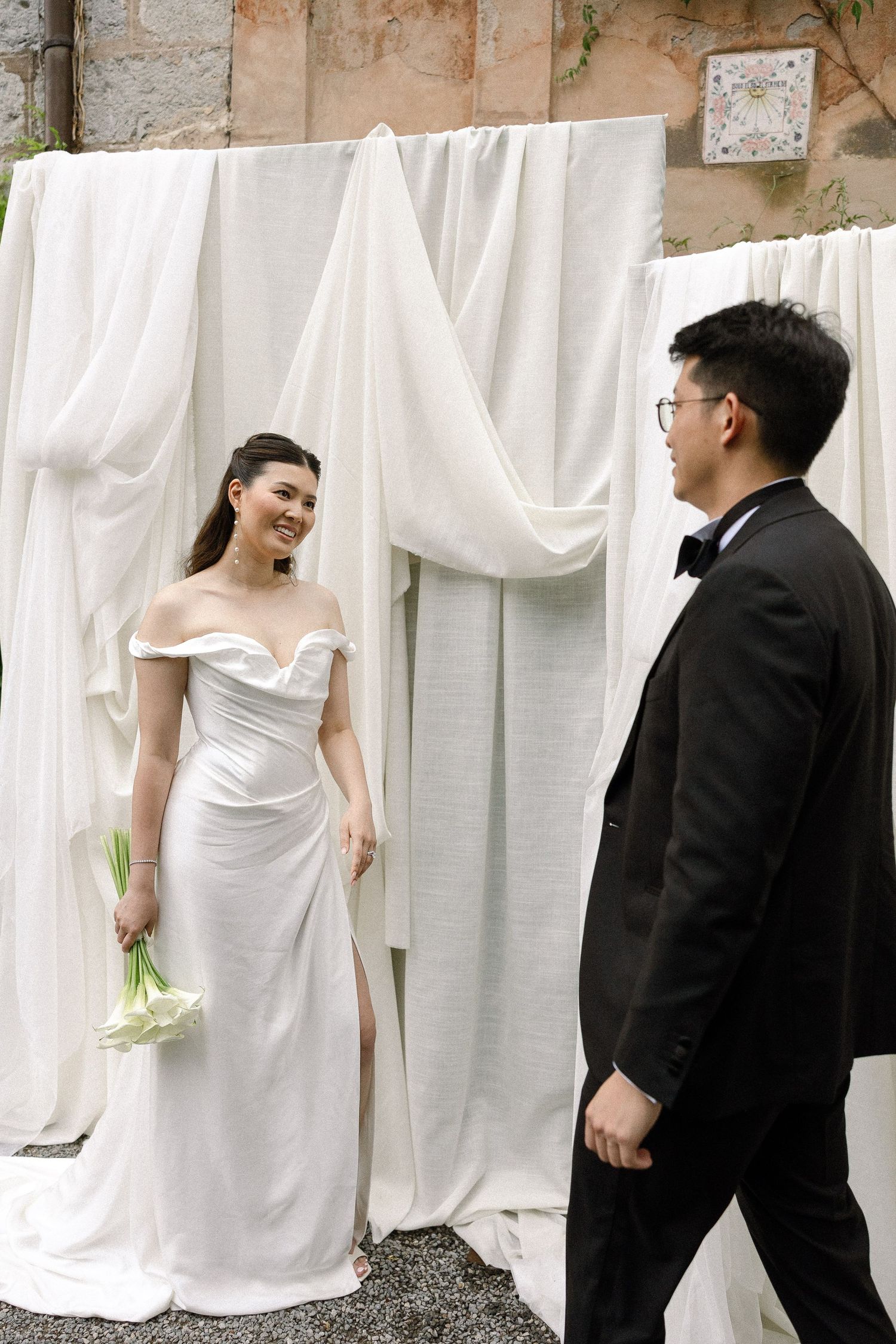 A couple poses against white fabric backdrop in formal wedding attire.