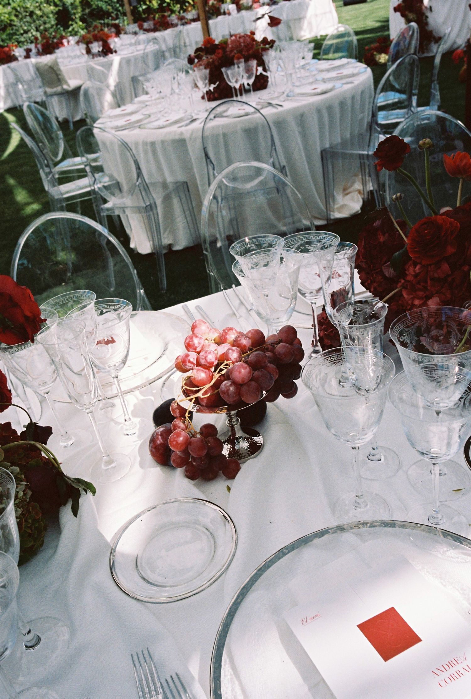 Elegant wedding reception table settings with white tablecloths, crystal glassware, and burgundy floral accents.