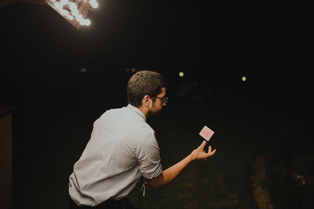 Magician in a white shirt performs a card trick in the dark.