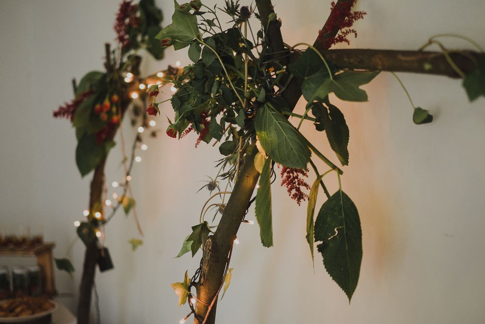 Elegant floral decorations with greenery and lights hanging from branches indoors.