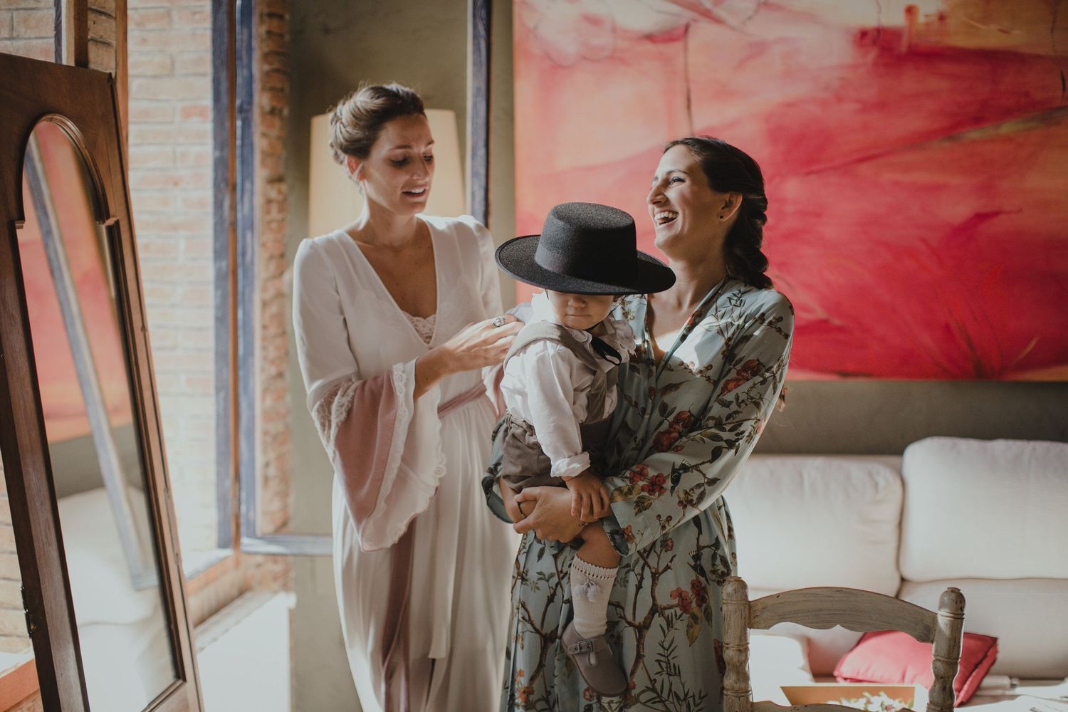 Three people share a joyful moment in a room with a pink abstract painting.