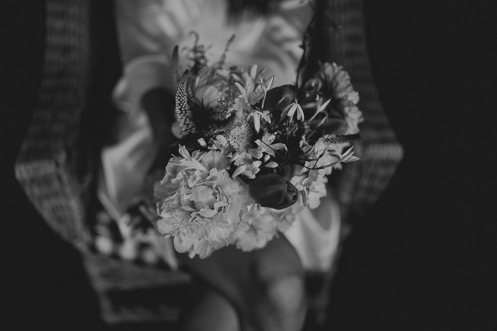 A delicate bouquet of mixed flowers held against light fabric in black and white.