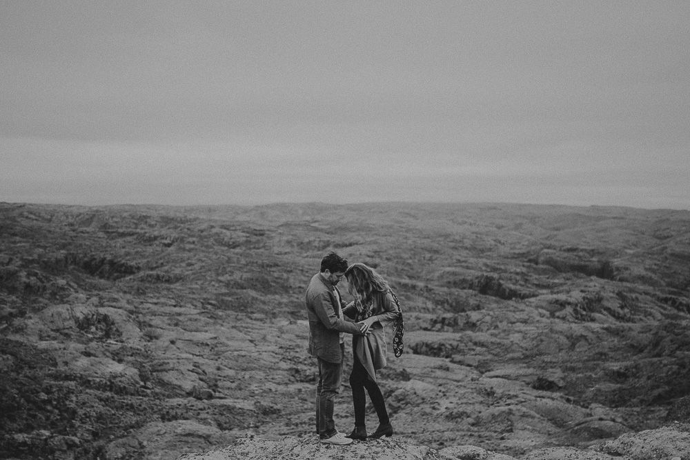 Intimate black and white photo of a couple embracing on a windswept hilltop.