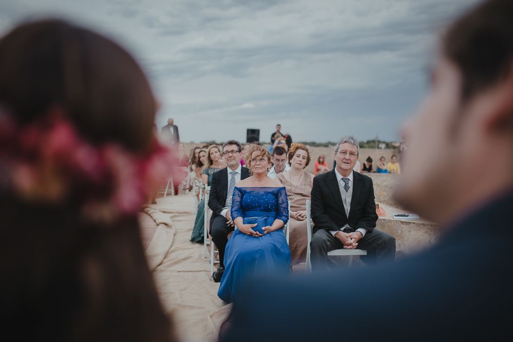 Wedding guests seated at an outdoor ceremony with cloudy skies in the background.