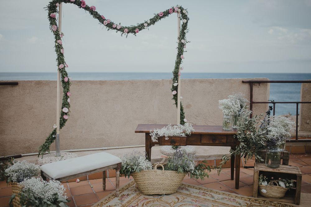 Wedding ceremony setup with floral arch and benches overlooking the ocean.