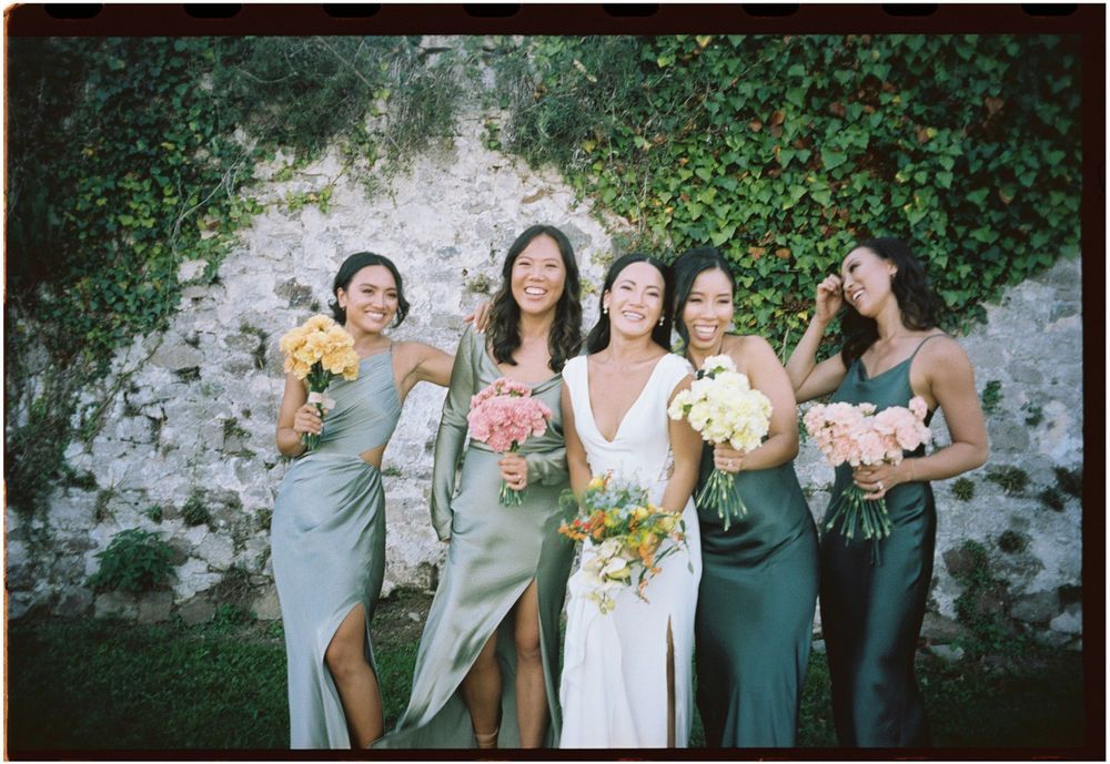 Wedding party in mix of sage green and neutral dresses posing together outdoors.
