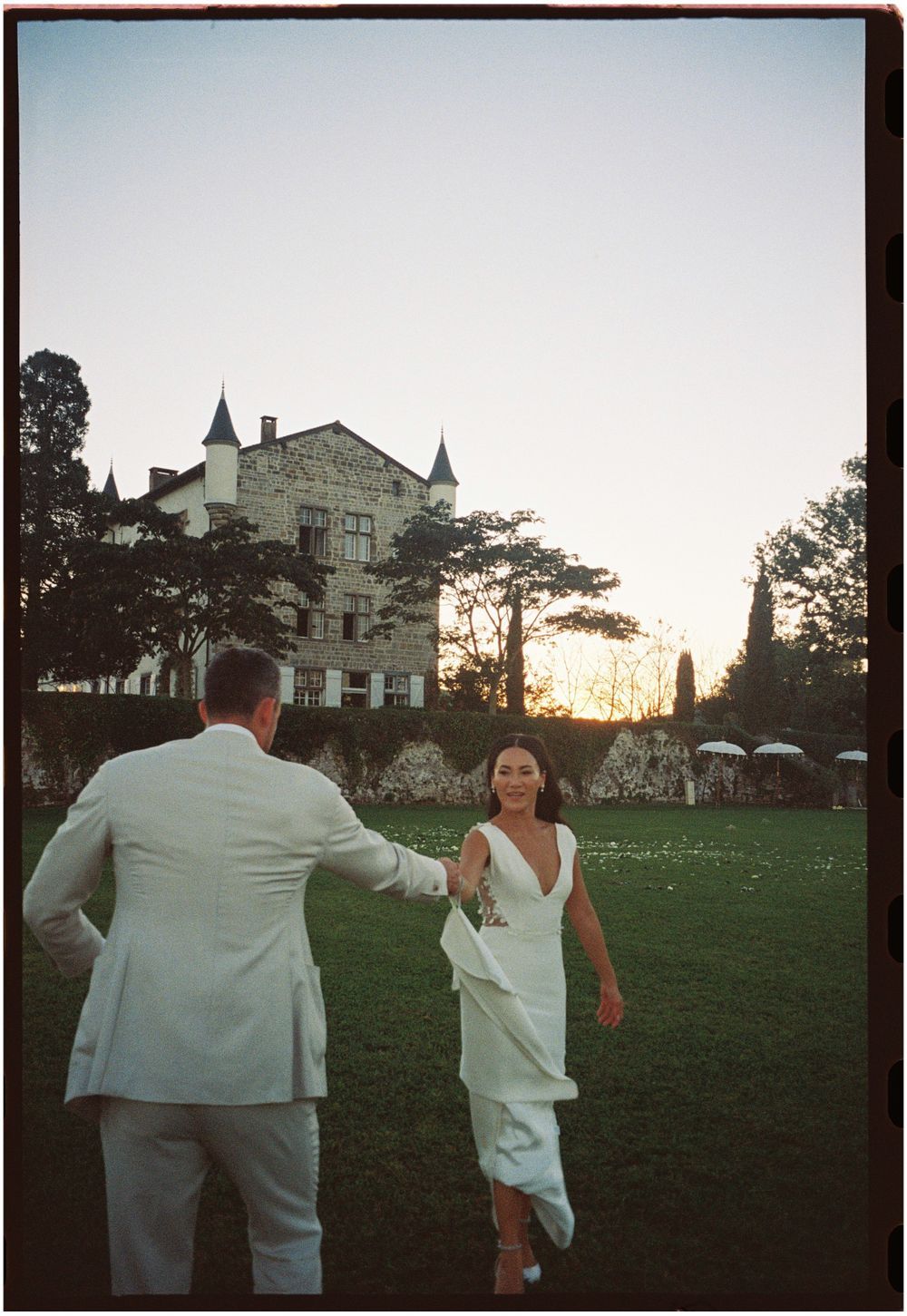 A sunset wedding moment on a grand estate lawn with a castle-like building in the background.