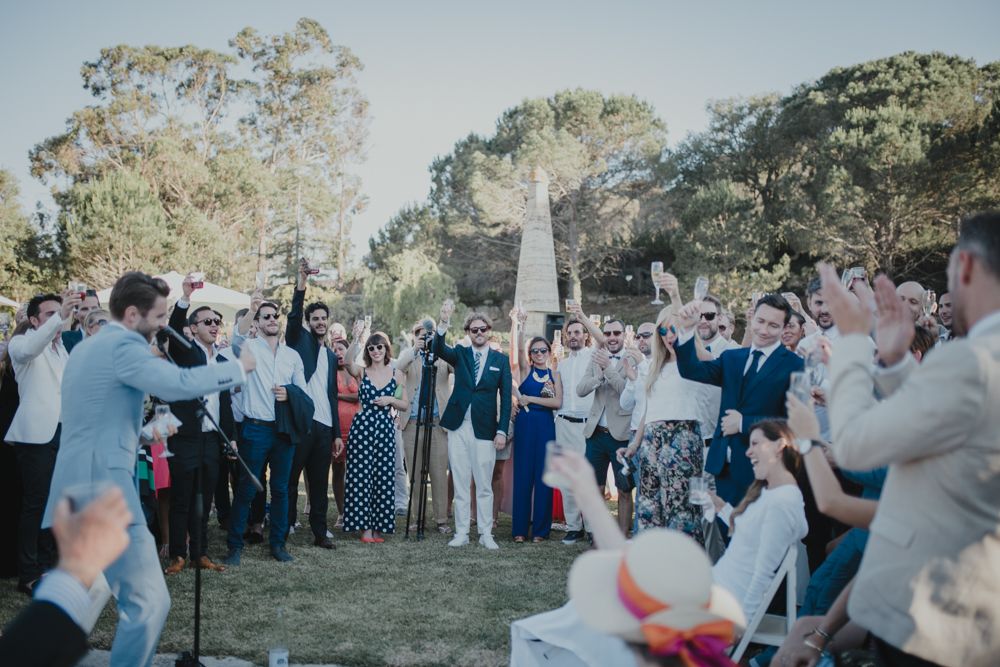 Guests celebrating at an outdoor wedding reception with trees in the background.